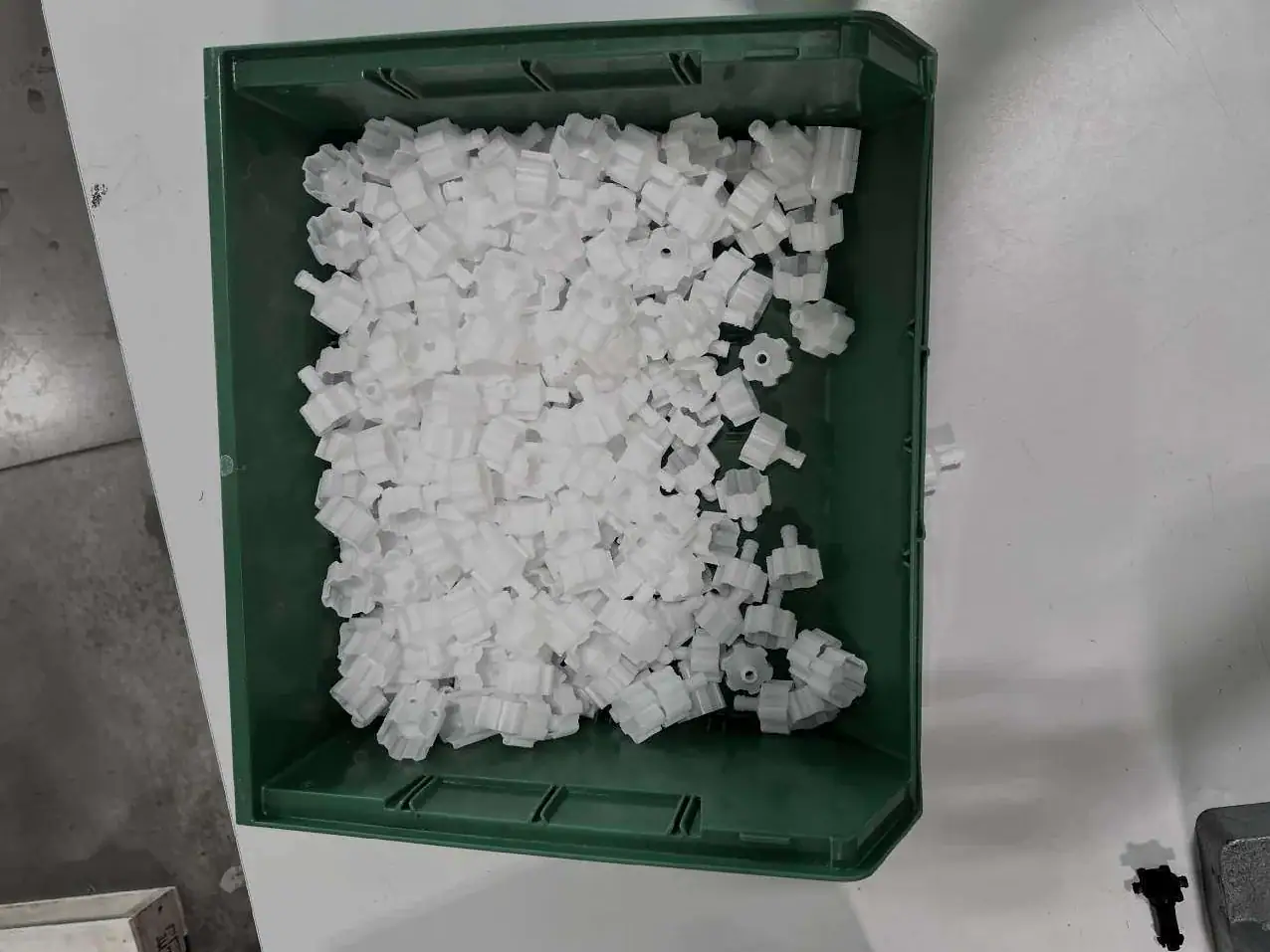 Green tote filled with white molded plastic parts on a workbench