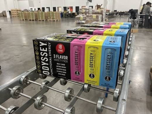 Three-flavor variety packs moving down a roller conveyor on the RELY floor