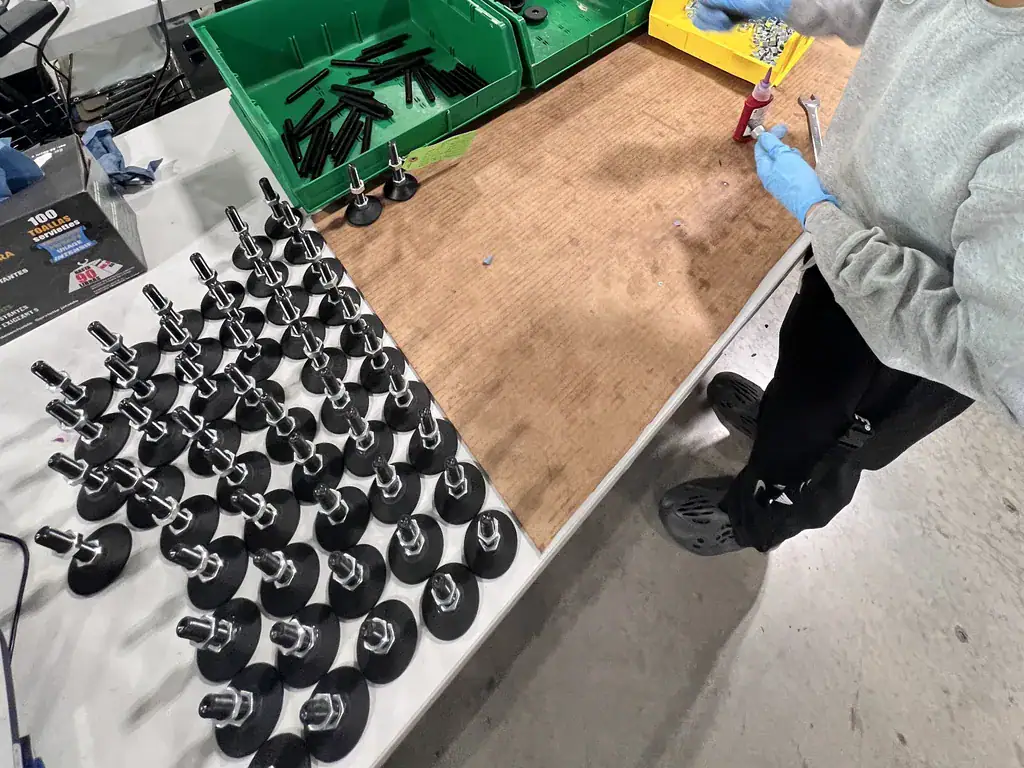 Rows of finished equipment feet on a workbench while a gloved RELY operator prepares the next one