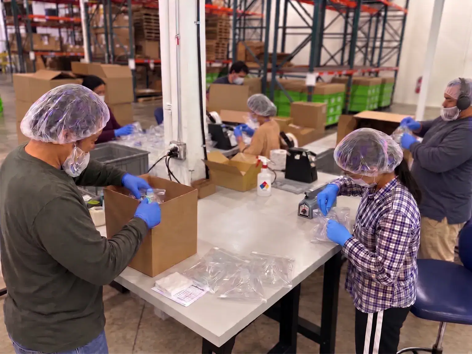 RELY team members in hairnets, face masks and gloves assembling, cleaning and bagging masks at a kitting table