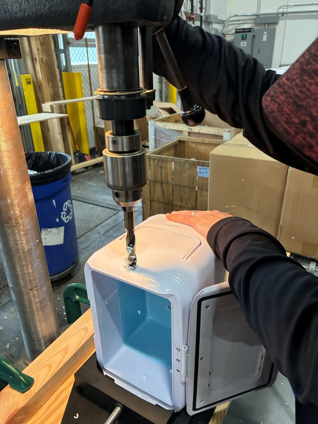 A RELY operator drilling a single hole in a mini fridge housing on a drill press